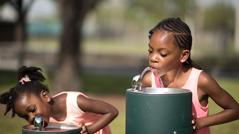 Two young girls drinking from water fountain