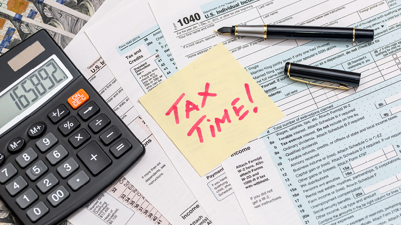Photo of tax forms, calculator, pen and a sticky note that reads "TAX TIME!"