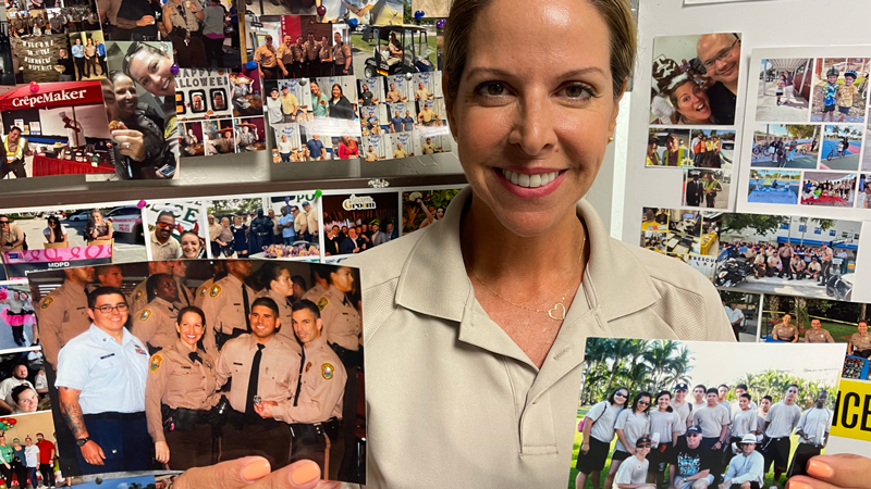 Officer Arlene Jimenez smiling while holding two photos for the camera of some of her former cadets