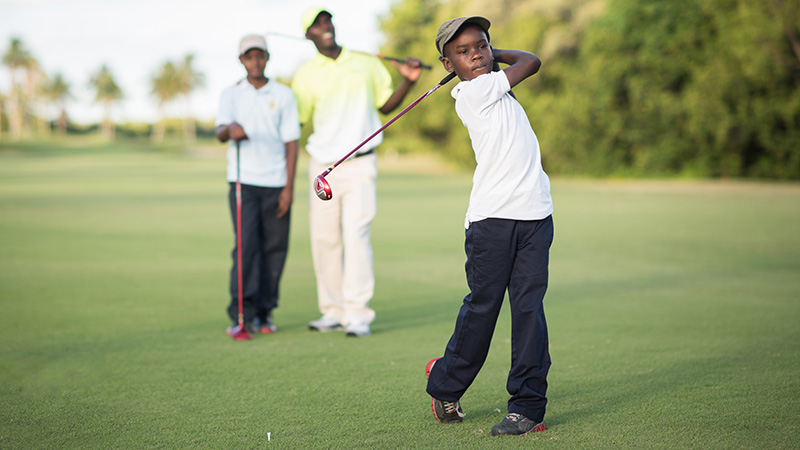 Boy swinging a golf club with father and brother watching behind him