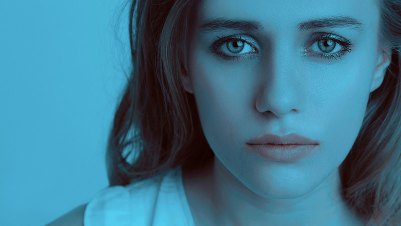 Woman looking sad in front of a solid blue background